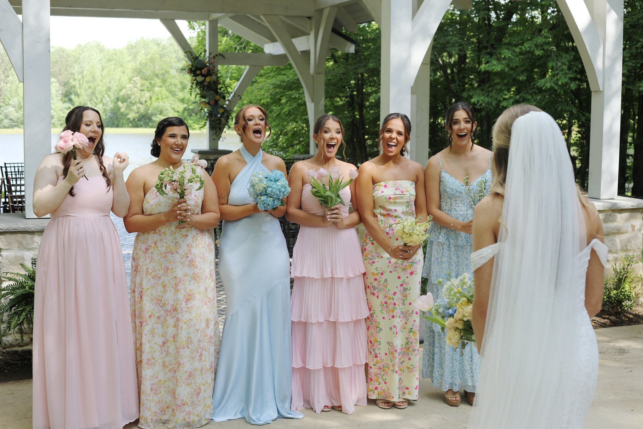 Bridesmaids in colorful dresses laughing with the bride outdoors.