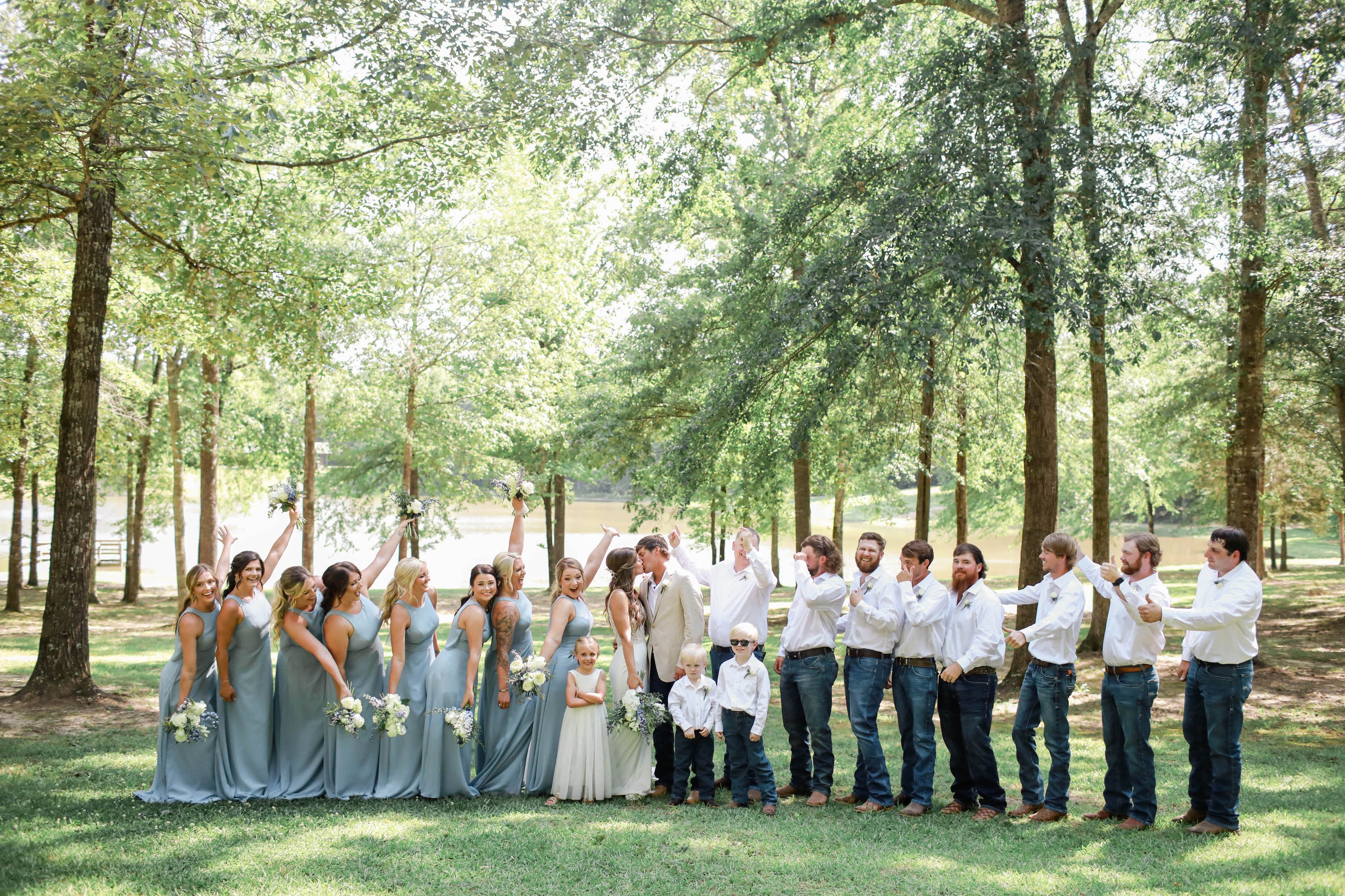 bridal party cheering while bride and groom kiss during wedding photos at Brookwood Venue
