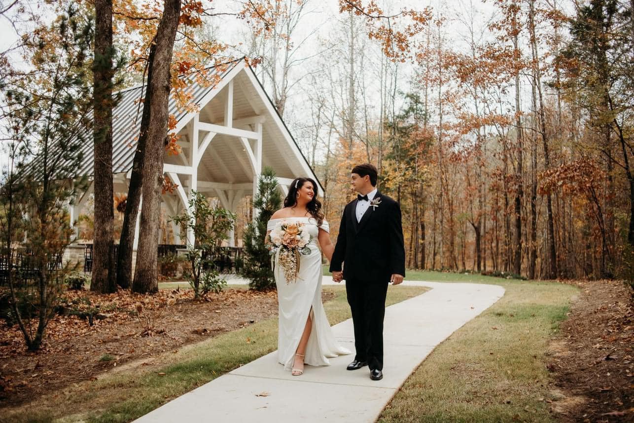 couple posing for wedding photos in for a fall wedding with outdoor chapel in the background