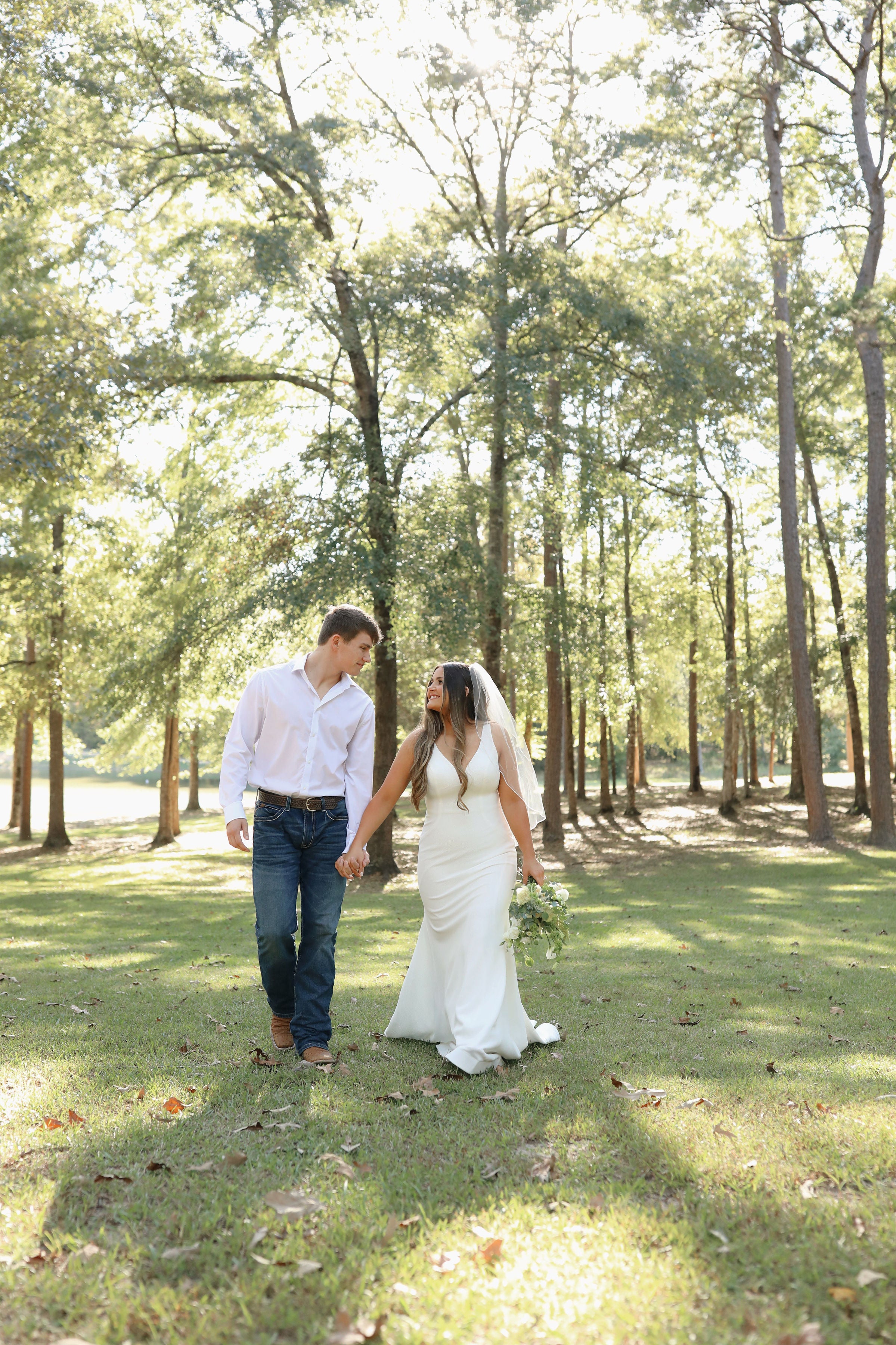 bride and groom holding hands walking through the woods at rustic venue in north mississippi