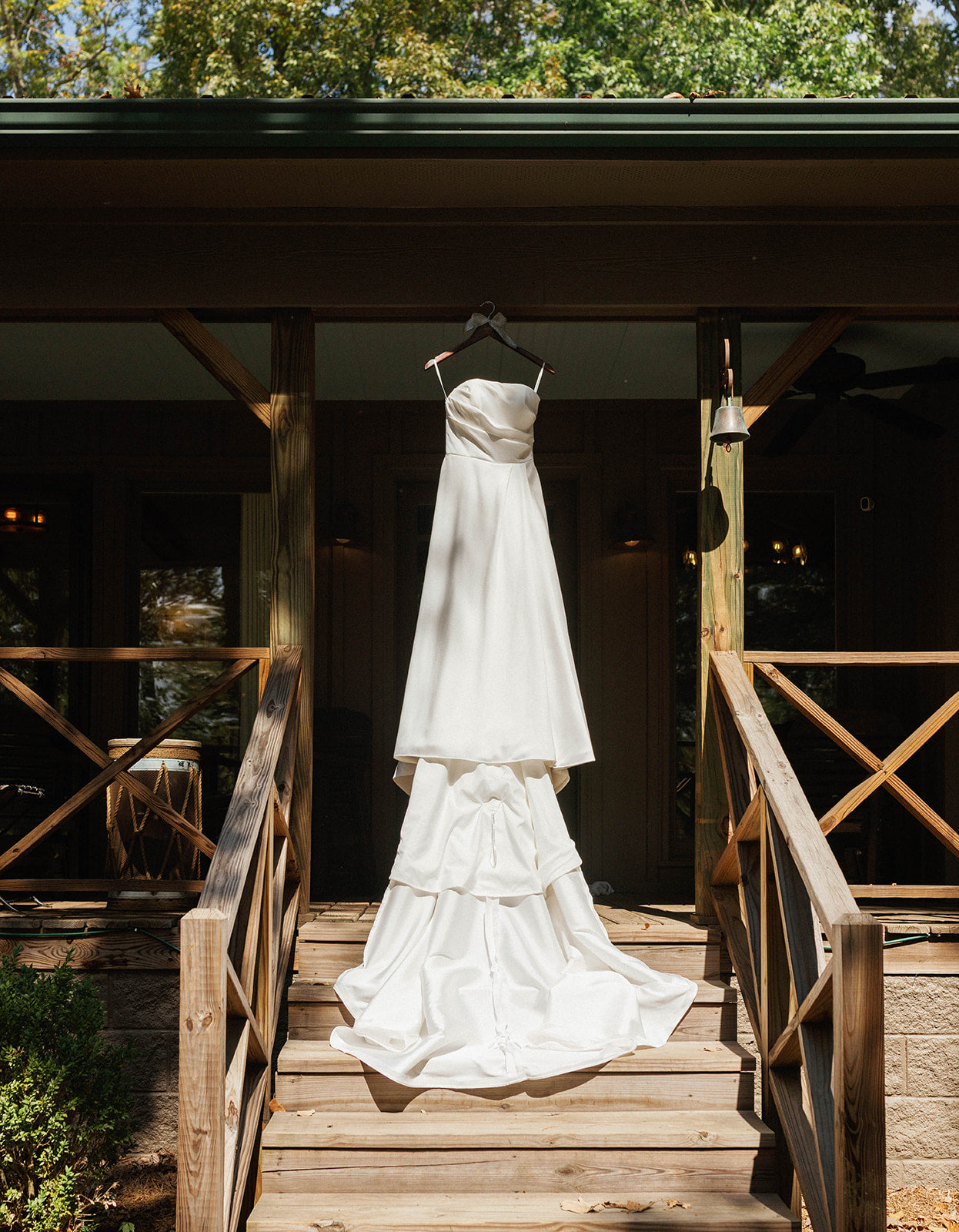 White wedding dress hanging on a wooden railing outdoors.